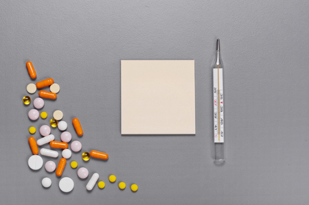 On a gray table paper for notes with a pills, capsules and thermometer