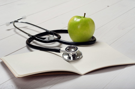 Closeup open notebook with blank pages with stethoscope and apple on a white doctor\'s table.の写真素材
