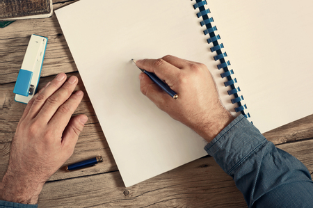 Men writes in an open notebook with blank pages on wooden desk closeup. Top view with copy spaceの写真素材