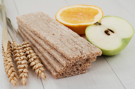 Dry diet crisp breads with ears of wheat, slice of apple and orange on a white wooden table closeup.の写真素材