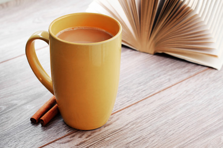 Coffee with milk in a large cup, standing on a wooden table nearby is cinnamon sticks and open bookの写真素材