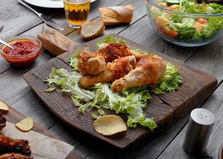Grilled chicken legs on lettuce leaves on a wooden massive board with sauceの写真素材