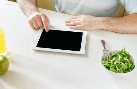 Man working using tablet computer while sitting at a white wooden table at homeの写真素材