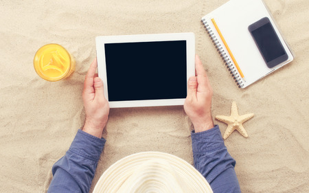 Man holding tablet with blank screen lying on the beach.の写真素材