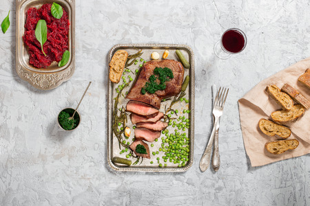 Sliced grilled beef steak on the old iron tray on light stone surface, top viewの写真素材