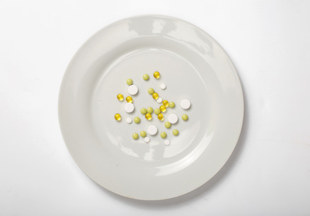 Different pills on a white plate on a white background, top view