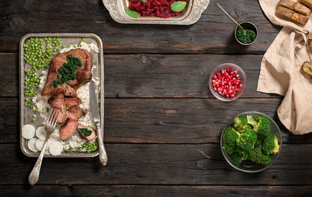 Frame with garnish of rice, salad of beets, broccoli, bread and sauce on a dark wooden tableの写真素材