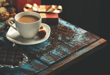 cup of coffee with variety of candy, chocolate bar and red gift box on wooden table with copy space