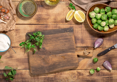 Around the wooden cutting board brussels sprouts and ingredients for cooking healthy and delicious food on a wooden table, top view. Healthy foodの写真素材