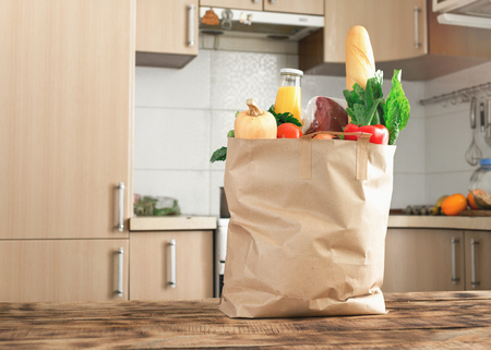 Paper bag full of healthy food on a wooden table in the kitchen close up with copy spaceの写真素材