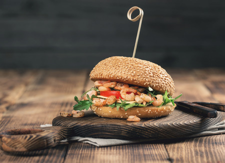 Burger with grilled shrimp, arugula, tomato and cheese on wooden board close up with copy spaceの写真素材