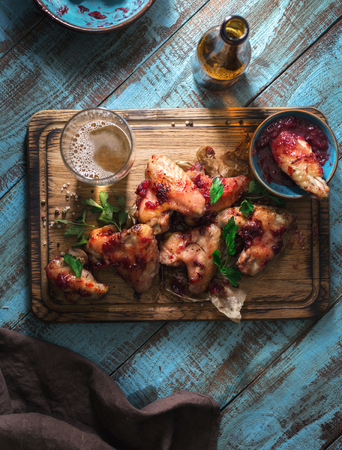 Chicken wings in cranberry sauce served on wooden board with lager beer, top viewの写真素材