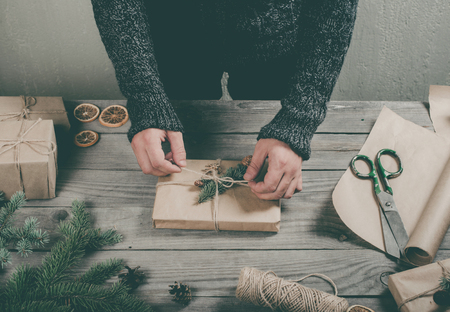 Male hands wrapping Christmas gift on wooden table close upの写真素材