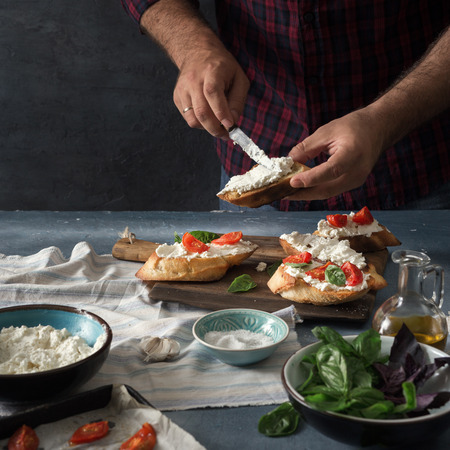 Man preparing an Italian bruschetta with baked tomatoes, basil and cheese on wooden boardの写真素材