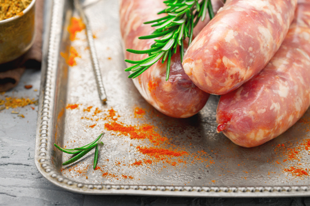 Raw sausages for grilling close up on tray with rosemaryの写真素材