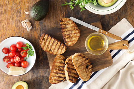 Top view Italian bruschetta with tomatoes, avocado and cheese on crusty grilled bread. Ingredients for cooking Italian bruschetta on dark tableの写真素材