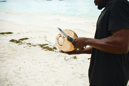 African man peels coconut on the beachの写真素材