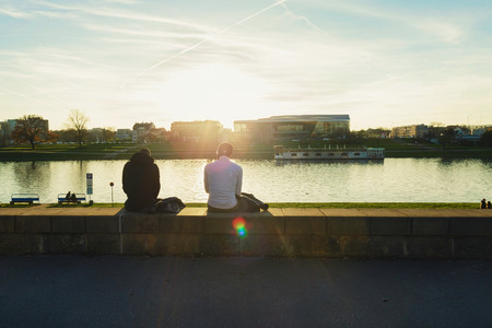 Two men sitting on city's embankment Krakow, enjoying the sunsetの写真素材