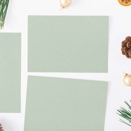 Flat lay christmas background. Empty cards with branch of Christmas tree, pine cones, dry orange and Christmas balls on white background, top viewの写真素材