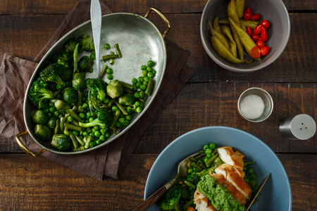 Roasted French bean, Brussels sprouts, green peas and chicken breast on a dark wooden background, top viewの写真素材