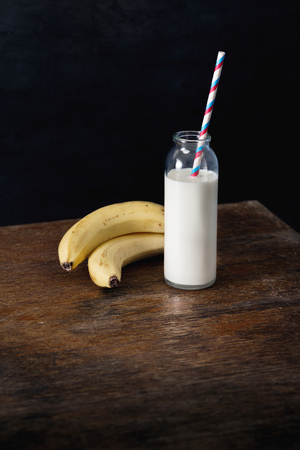 Bottle of milk with banana on dark wooden table. Healthy breakfast conceptの写真素材