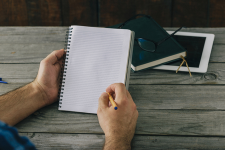 Men's hands write in a notebook on a wooden table. Home Workplaceの写真素材