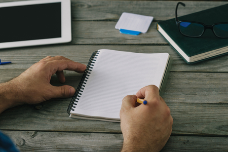 Close up male hands write in notebook on wooden table. Home Workplaceの写真素材