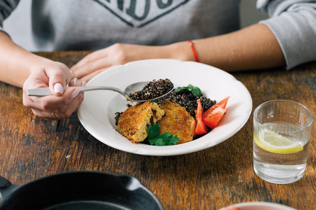 Healthy vegetarian food concept. Woman eating vegetarian food (black quinoa and cutlets from oatmeal and prunes) on wooden tableの写真素材