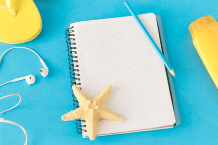Notepad with pencil and beach accessories on a blue background