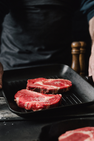 Male hands holding a grill pan with beef steaks on kitchen Man cooking beef steaksの写真素材