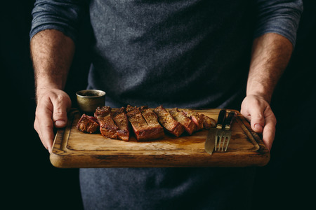 Man holding juicy grilled beef steak with spices on cutting boardの写真素材