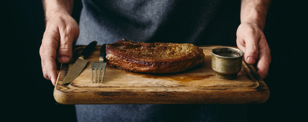 Man holding grilled beef steak with spices on cutting boardの写真素材