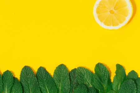 Creative summer background. Grass made of green mint leaves and sun of lemon on yellow background top view. Minimal summer concept. Flat layの写真素材