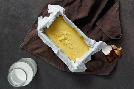 Raw dough for cooking corn bread in baking cookware on dark background top view