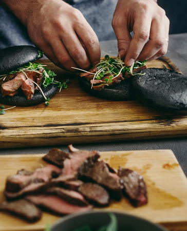 Man cooking burgers with grilled meat on wooden board close upの写真素材