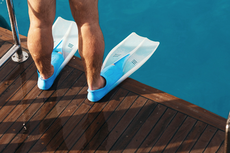 Male legs in flippers close up on the deck of yacht