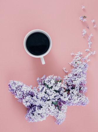 Top view spring minimal concept. Flat lay cup of coffee with branches of lilac flowers on pink backgroundの写真素材