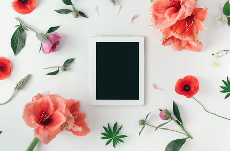 Flat lay tablet computer with blank screen on white background with wildflowers, poppy, amaryllis, peonies, top viewの写真素材
