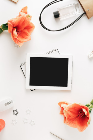 Flat lay, top view office table desk. Feminine desk workspace with flower amaryllis, tablet, notebook, pen, computer mouse, bag and female perfume on white backgroundの写真素材
