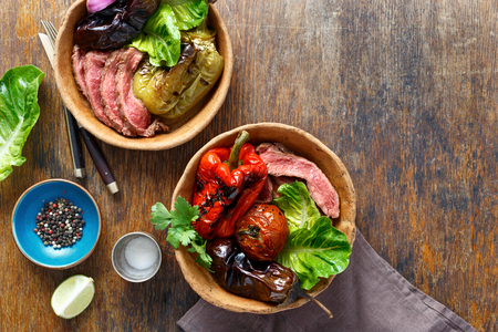 Grilled steak with grilled vegetables served in bread plate on wooden table with copy space, top viewの写真素材