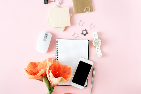 Flat lay, top view office table desk. Feminine desk workspace with flower amaryllis, notebook, pen, smartphone, computer mouse and womens on pink backgroundの写真素材