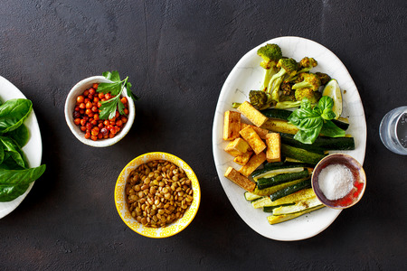 Healthy food clean eating source of protein for vegetarians: Baked vegetables (zucchini and broccoli), roasted tofu cheese roast chickpeas and green lentils on dark background, top view. Healthy food conceptの写真素材