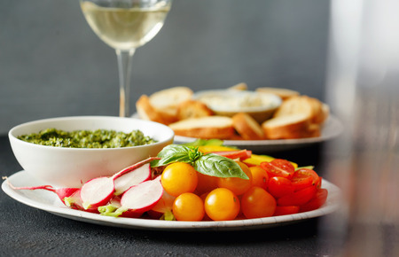 Healthy snacks for wine. Vegetables, bread croutons with pesto sauce and garlic sauce on black stone background with white wineの写真素材