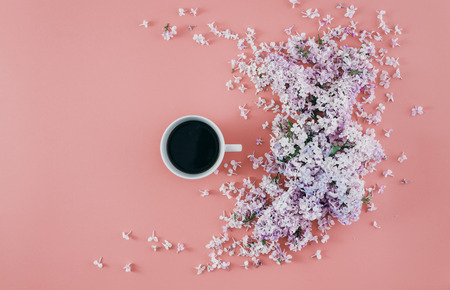 Lilac flowers with cup coffee on pink background. Minimal floral flat lay concept. Flat lay, top viewの写真素材