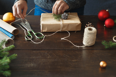 Wrapping presents background. Male hands wrapping gift box on wooden table. Rustic Christmas...
