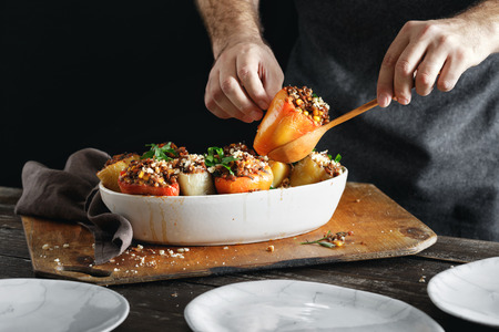 Male hands holding cooked stuffed peppers with green lentils, sweet corn, salsa and almonds on...