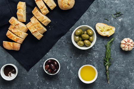 Italian food concept. Cooking Italian bruschetta. Olives, fresh baguette slices, olive oil, garlic and rosemary on dark stone background top viewの写真素材