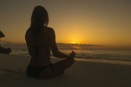 Women do meditation on the ocean beach at sunsetの写真素材