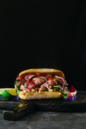 Grilled spicy steak sandwiches steak in fire flame on wooden cutting boards on dark background close upの写真素材