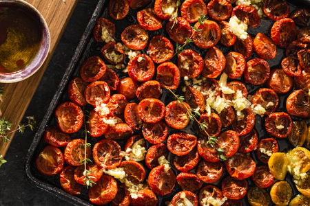 Baked juicy cherry tomatoes into a baking tray on dark background top viewの写真素材